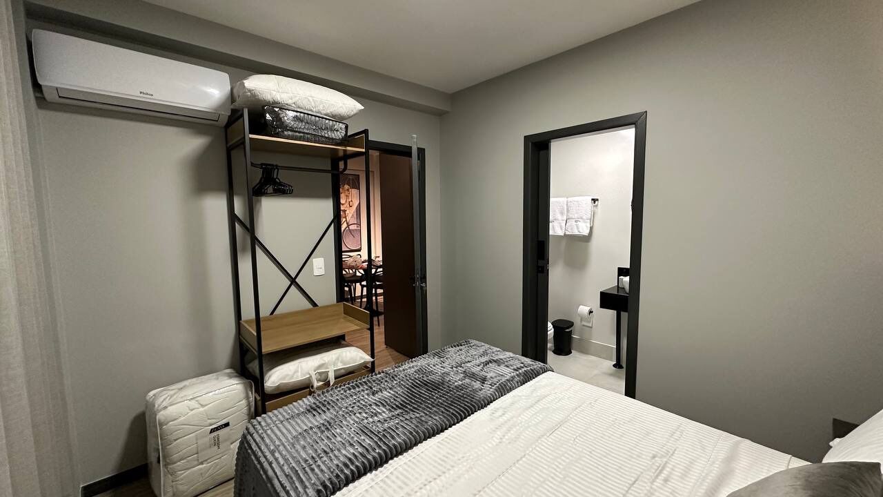 A compact hotel room with a bed, a small desk, a wardrobe, and a built-in bench.