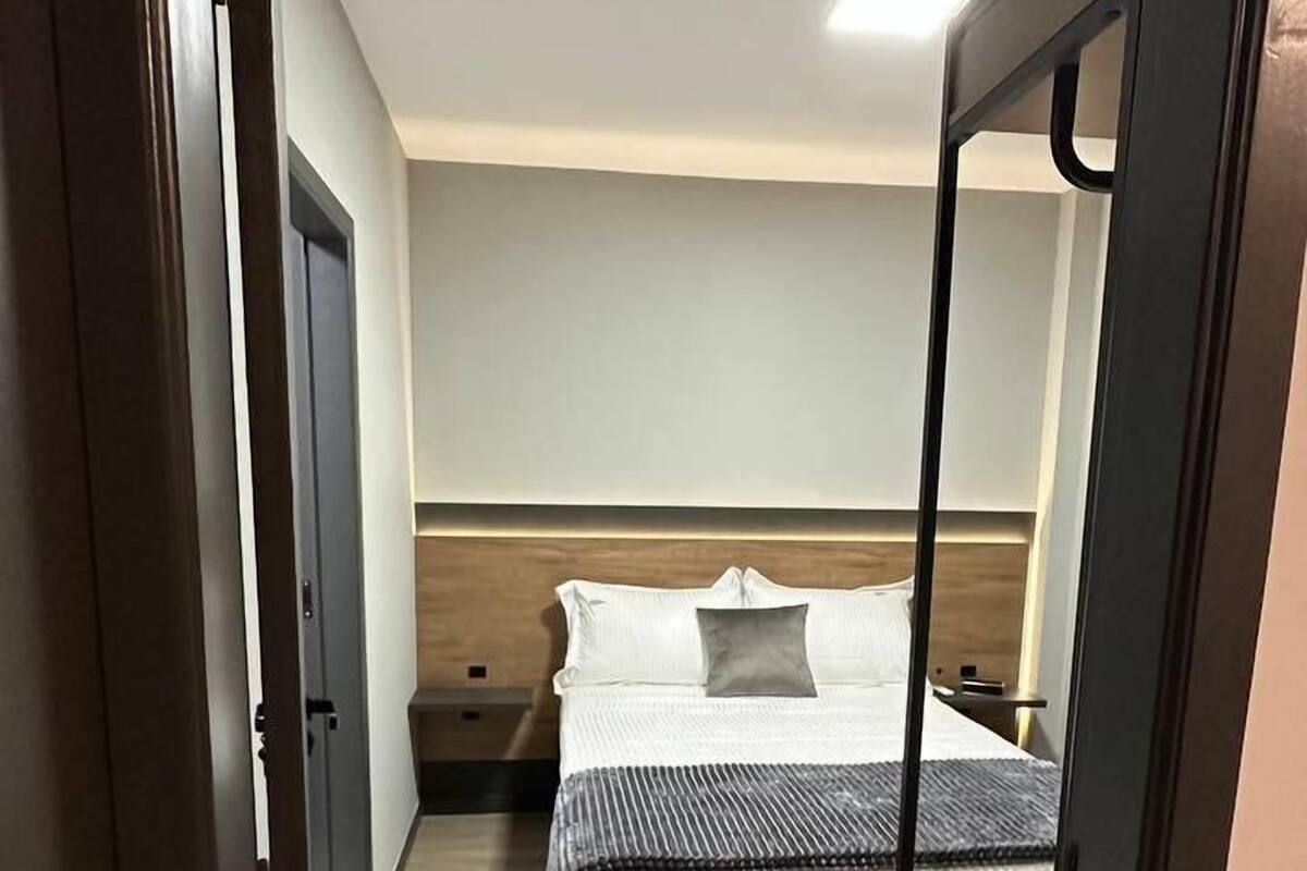 A narrow hallway leading to a bedroom with a bed, nightstands, and a wooden headboard.