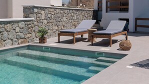 A pool area with two lounge chairs, a stone wall, and a potted plant. - Velonis Villa, Velonis Villas (Naxos)