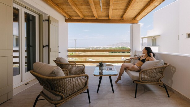 A balcony with wicker furniture, a table, and a person relaxing. - Velonis Villa, Velonis Villas (Naxos)