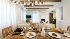 A dining table set with breakfast items, a TV in the background, and a modern interior design. - Velonis Villa, Velonis Villas (Naxos)