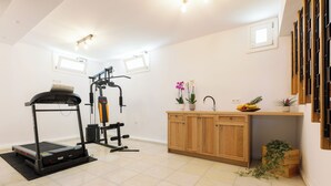 A gym with a treadmill and weight machines, a wooden cabinet with a sink, and a small window. - Velonis Villa, Velonis Villas (Naxos)