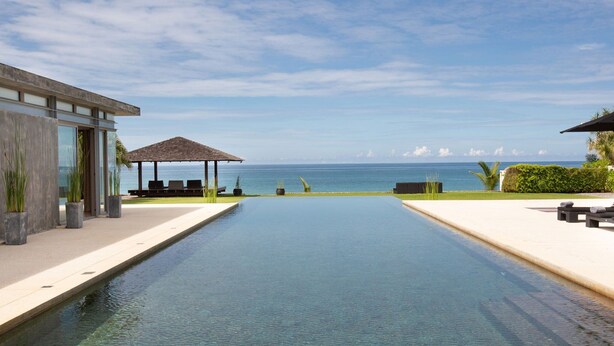 A modern infinity pool with a clear view of the ocean, a covered seating area, and a building with large windows. - Luxe Vacay Beachfront Sava Villa 4 | Villa Essenza | Chef & Staff | LTH-15 (Takua Thung)