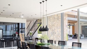 A modern kitchen with a glass dining table, black chairs, and a stone accent wall. - Luxe Vacay Beachfront Sava Villa 4 | Villa Essenza | Chef & Staff | LTH-15 (Takua Thung)