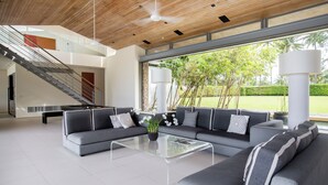 A modern living room with a grey sectional sofa, a glass coffee table, and a staircase leading to an upper level. - Luxe Vacay Beachfront Sava Villa 4 | Villa Essenza | Chef & Staff | LTH-15 (Takua Thung)