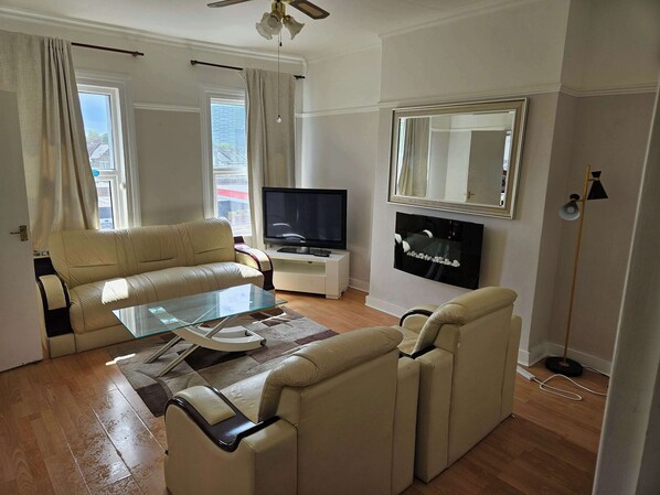 A living room with a sofa, a glass coffee table, a television, a fireplace, and a large mirror.