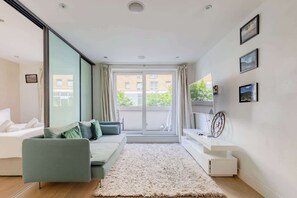 Un salon moderne avec un canapé, un tapis blanc, un téléviseur et une grande fenêtre avec des rideaux.