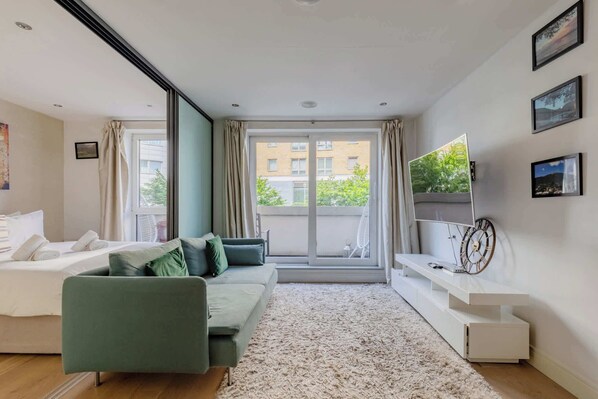 A modern hotel room with a sofa, a TV, a large window, and a view of buildings outside.