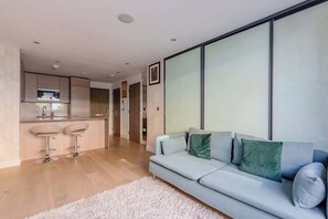 A modern living room with a sofa, a white fluffy rug, and a kitchen area with bar stools.