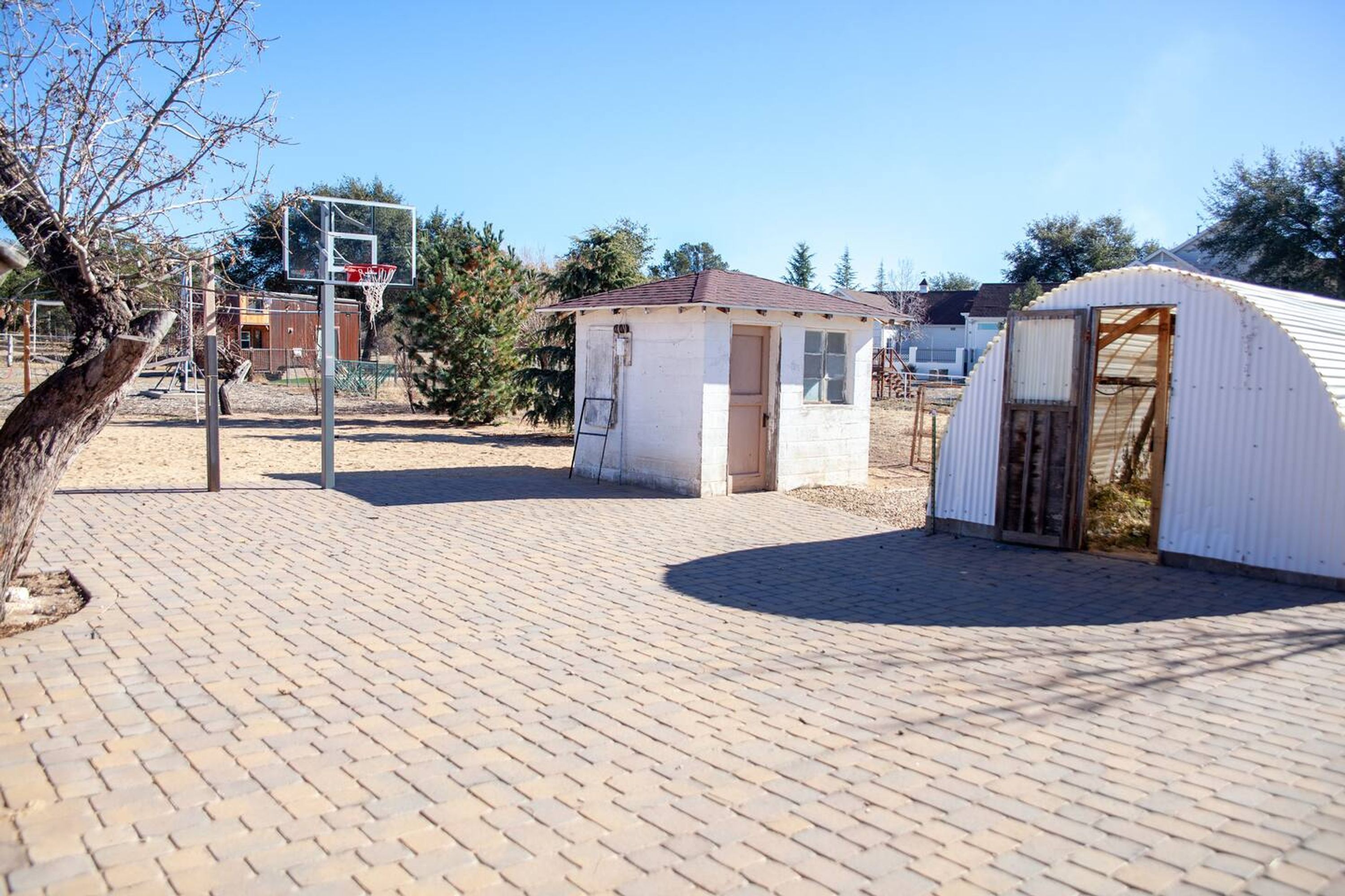 A brick-paved area with a basketball hoop, a small shed, and a large tent-like structure.