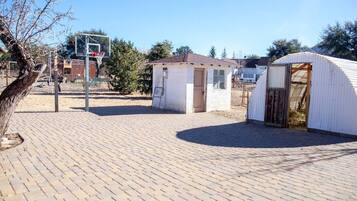 A brick-paved area with a basketball hoop, a small shed, and a large tent-like structure.