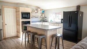 Una cocina moderna con una isla central, taburetes de bar, un refrigerador negro y armarios de madera.