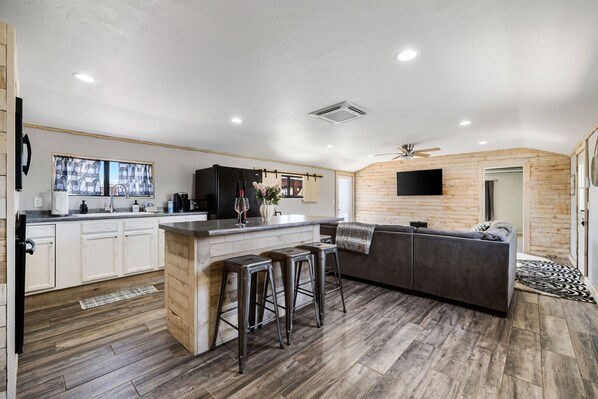 Una cocina moderna con una isla central, taburetes de bar, un refrigerador empotrado y un amplio ventanal.