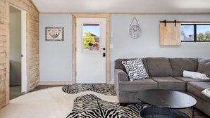 Una sala de estar con una pared de madera, un sofá, una mesa de centro, un tapete estampado con motivos de cebra y un reloj en la pared.