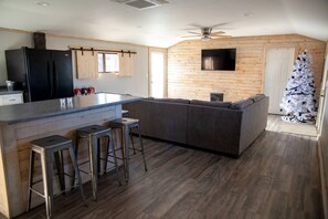 Una cocina moderna con una isla central, taburetes de bar, un refrigerador integrado y una pared de madera con un televisor montado.