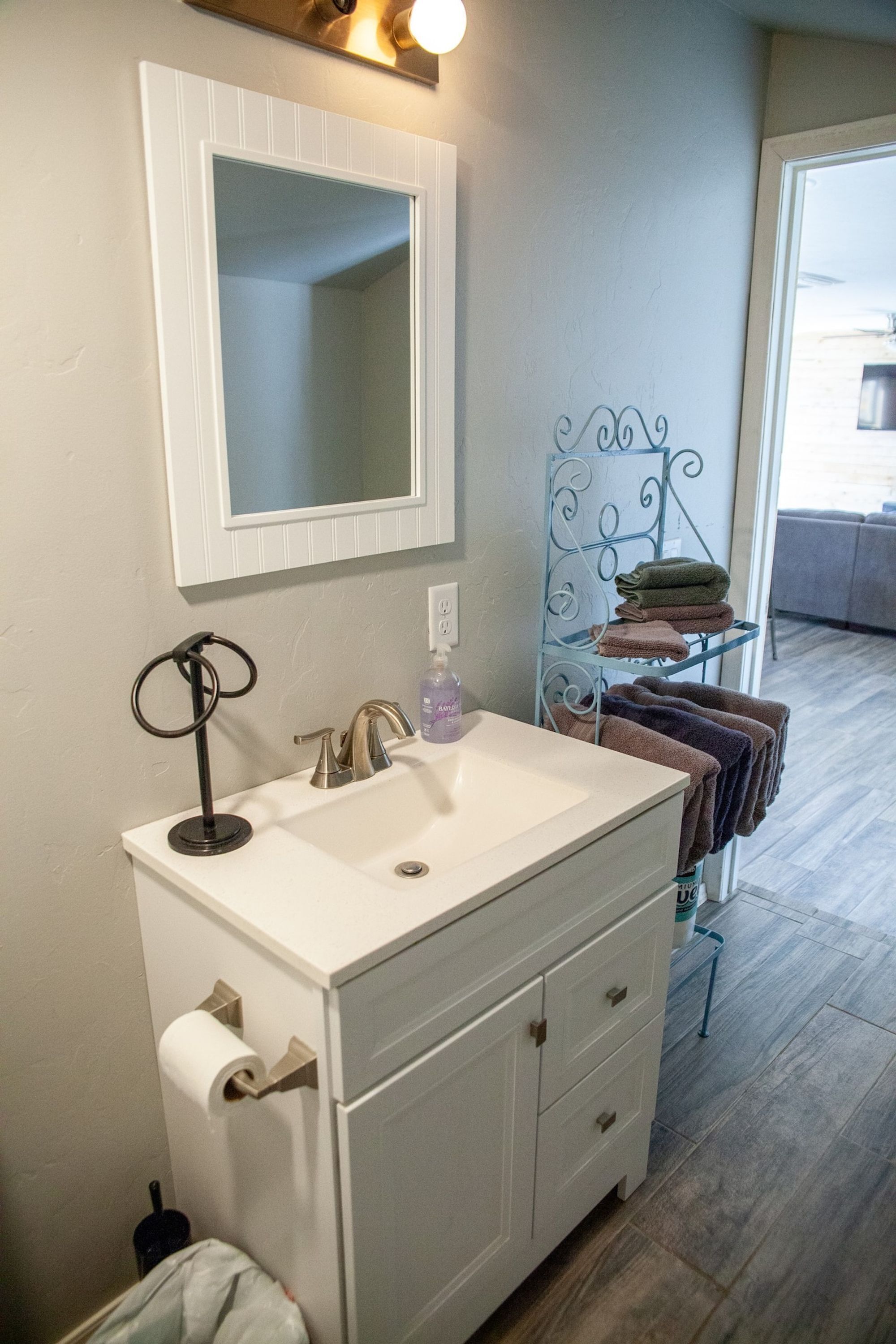 Une salle de bain avec un lavabo blanc, un miroir au-dessus et un porte-serviettes avec des serviettes pliées.