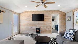 Una sala de estar acogedora con chimenea, ventilador de techo y televisor de pantalla plana montado en una pared de madera.