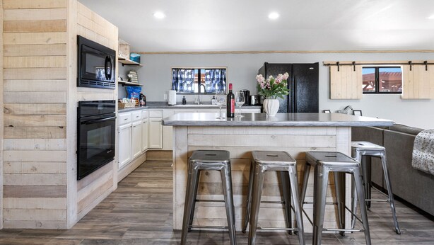 Una cocina moderna con detalles de madera, una isla central, taburetes de bar y un ventanal grande.