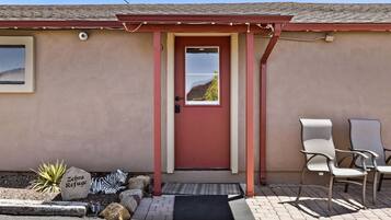 A building with a red door, a small window, and a sign reading "Zebra Refuge" on a rock. There are two chairs outside.
