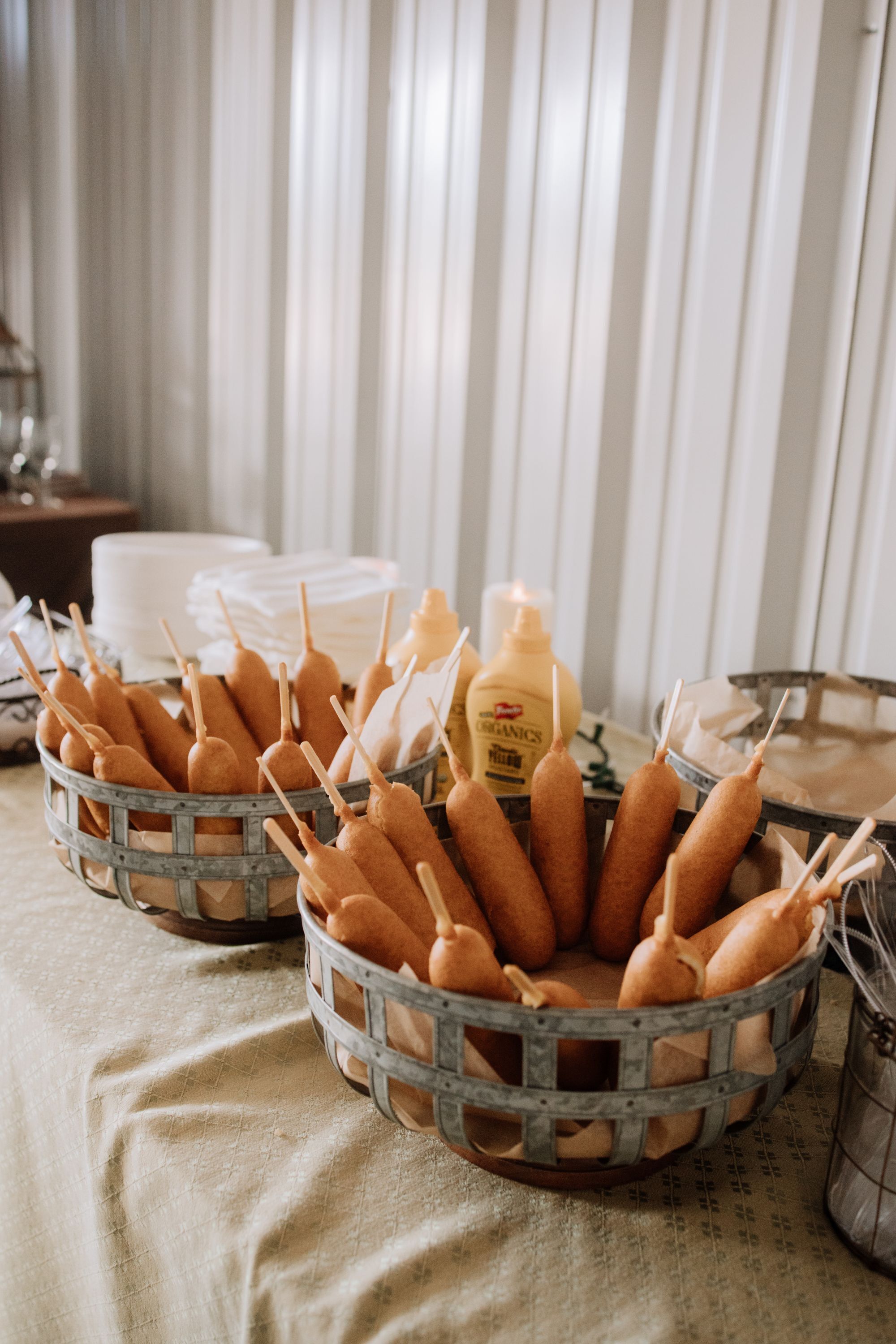 Two baskets of corn dogs on a table with a candle and a bottle of mustard.