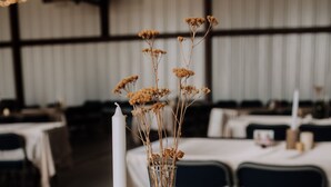 Une table avec une bougie, des fleurs séchées et un cadre photo.