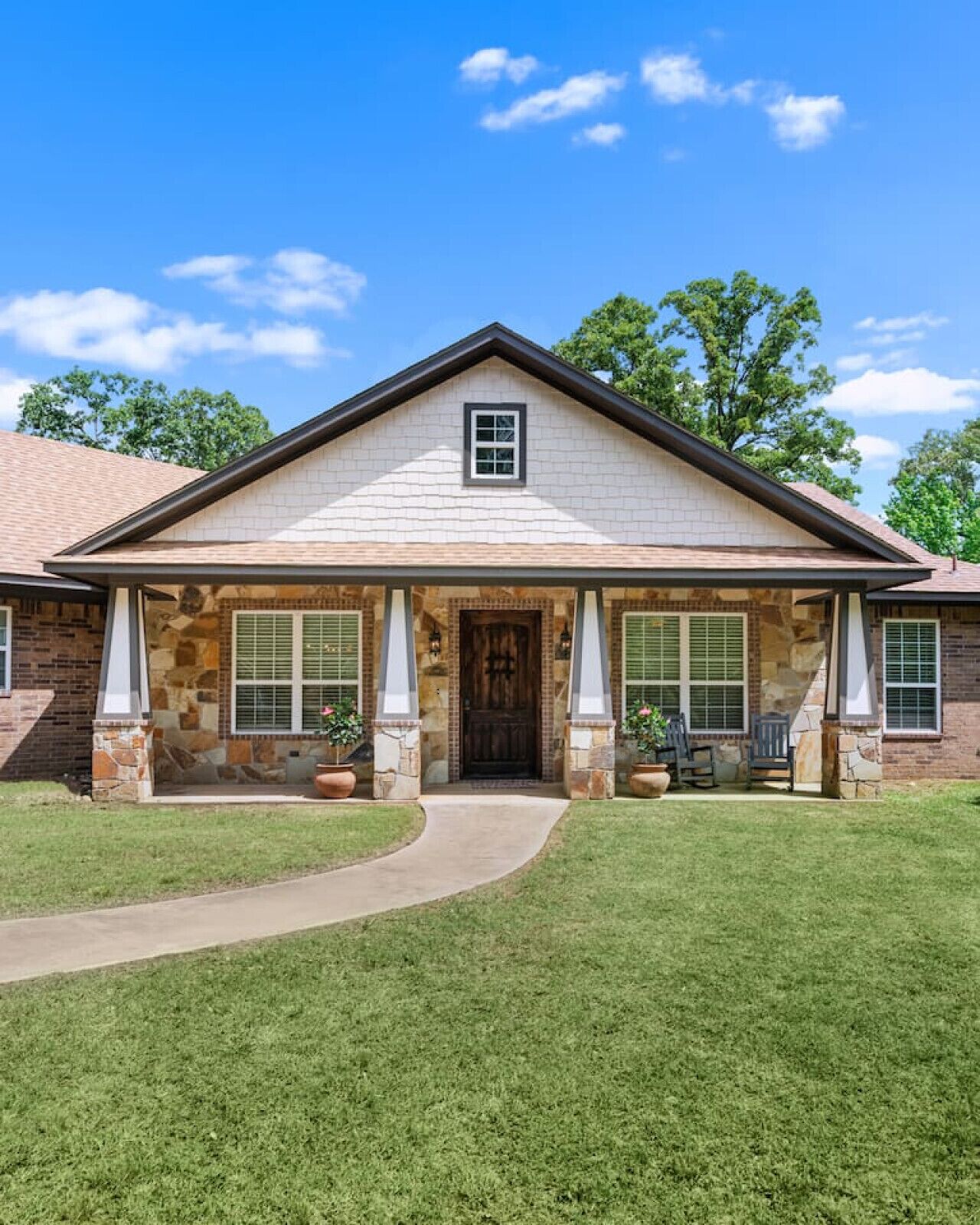 A two-story house with a stone facade, a front porch with columns, and a clear blue sky.