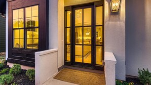 A house with a large window and a door illuminated by warm lighting.