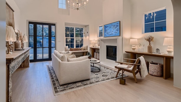 A spacious living room with a fireplace, large windows, and a chandelier.