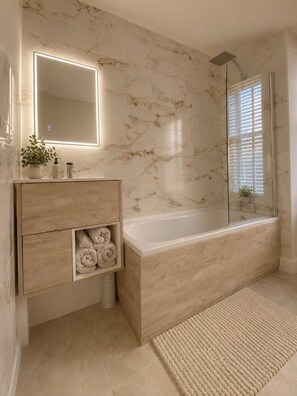 A bathroom with a marble wall, a wooden vanity, a bathtub, and a glass shower enclosure.