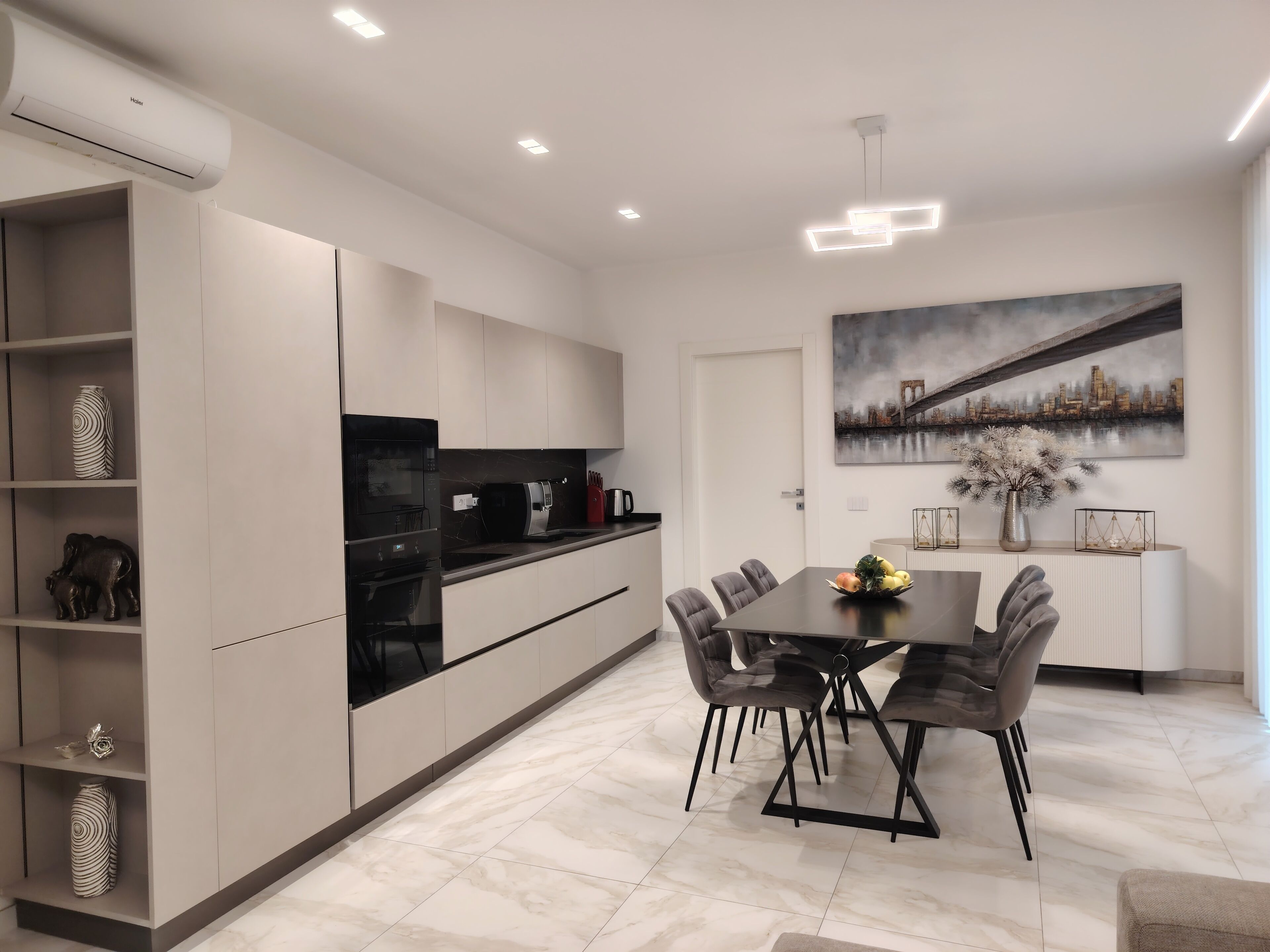Una cocina moderna con comedor, que incluye una isla grande, electrodomésticos integrados y un cuadro con vista a la ciudad.