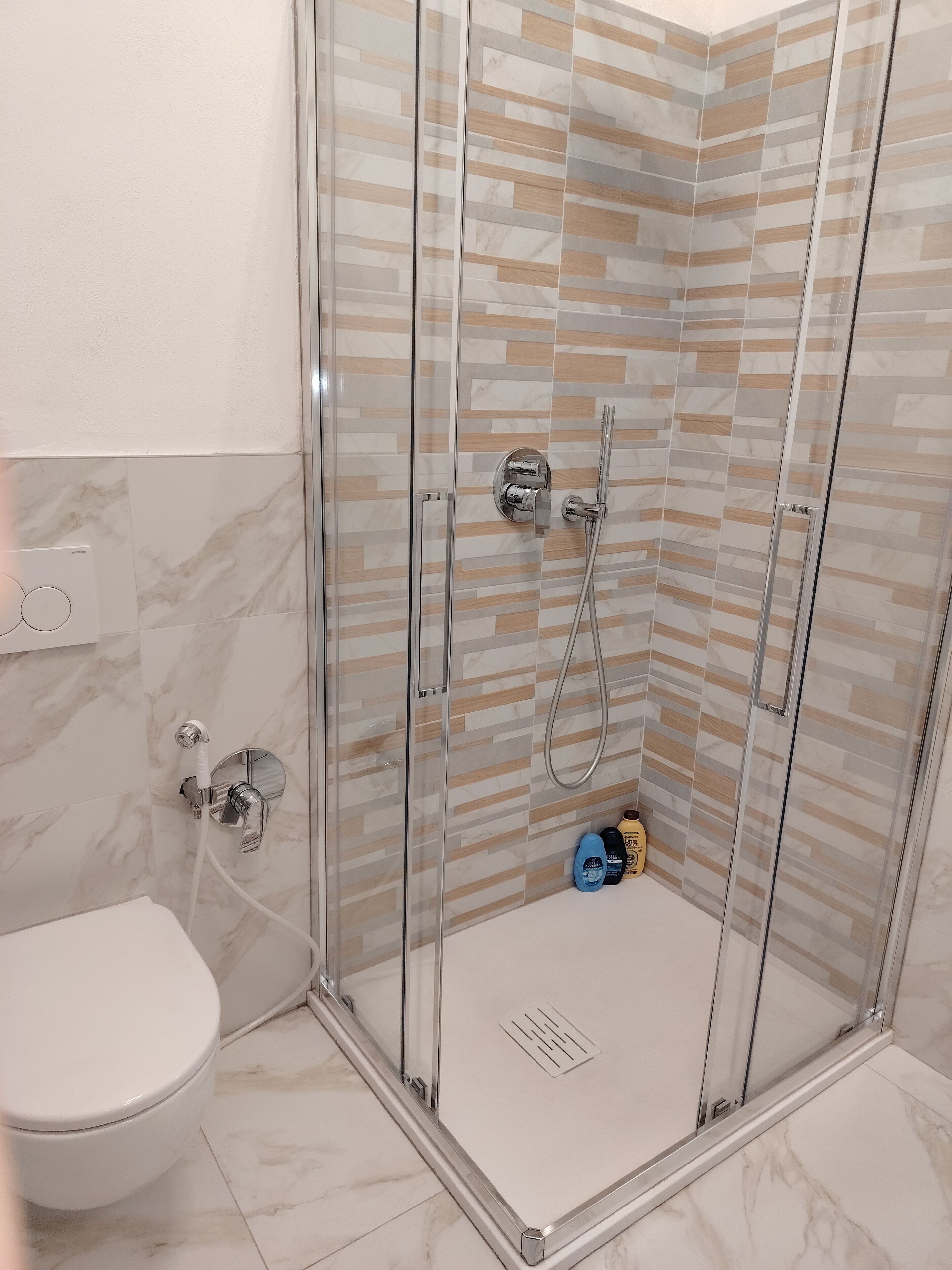 Een moderne badkamer met een glazen douchecabine, een toilet en een vloer van marmeren tegels.