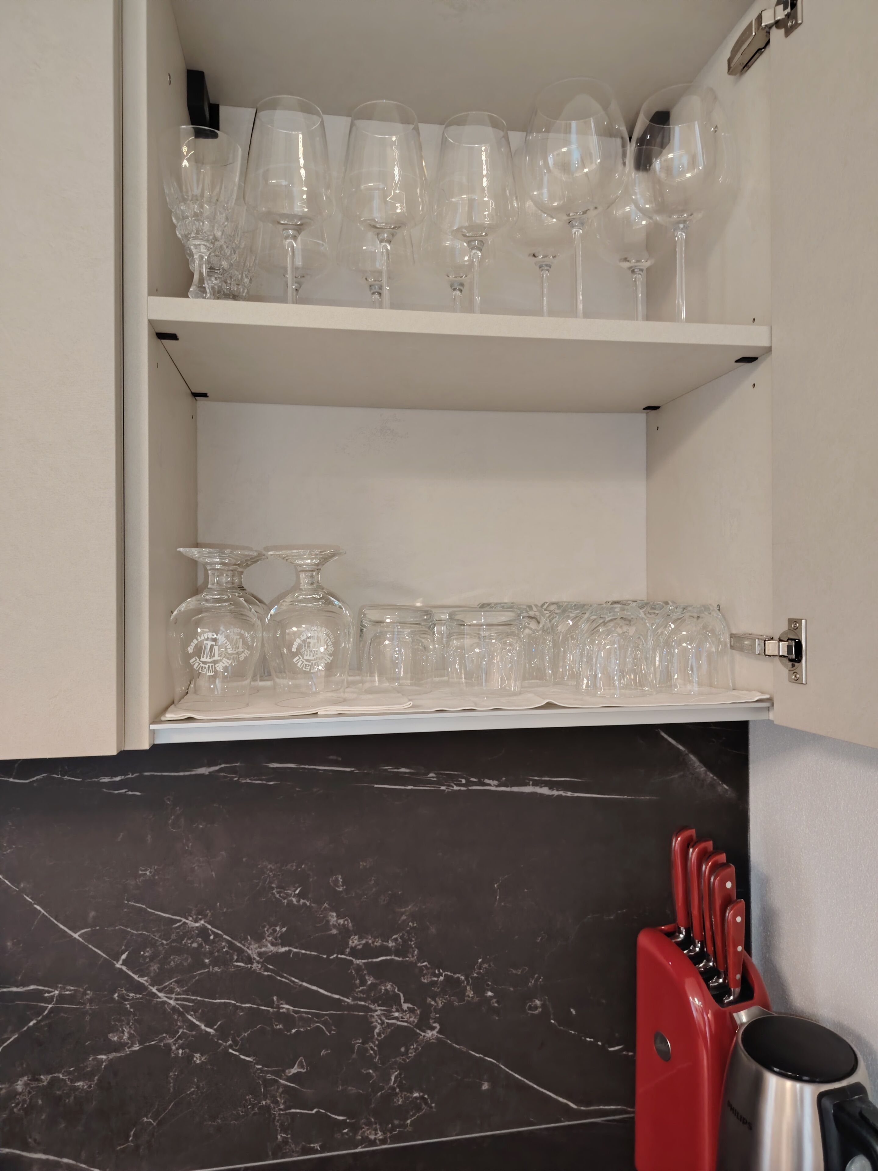 Eine Küche mit einer Marmorarbeitsplatte, einem roten Messerblock und Regalen für Weingläser und Trinkgläser.