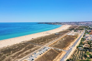Vista aérea de uma área costeira com praia, estacionamento e edifícios residenciais.