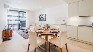 A modern dining area with a round table set for four, a sofa, and a kitchen with white cabinets. - Santa Maria II Pool View (SR 1-B2.0O) (Lagos)