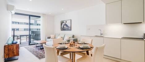 Un comedor moderno con una mesa redonda para cuatro, un sofá y una cocina con armarios blancos.