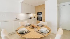 A modern kitchen with white cabinets, a microwave, and an oven. There is a dining table set with plates, glasses, and cutlery. - Santa Maria II Pool View (SR 1-B2.0O) (Lagos)