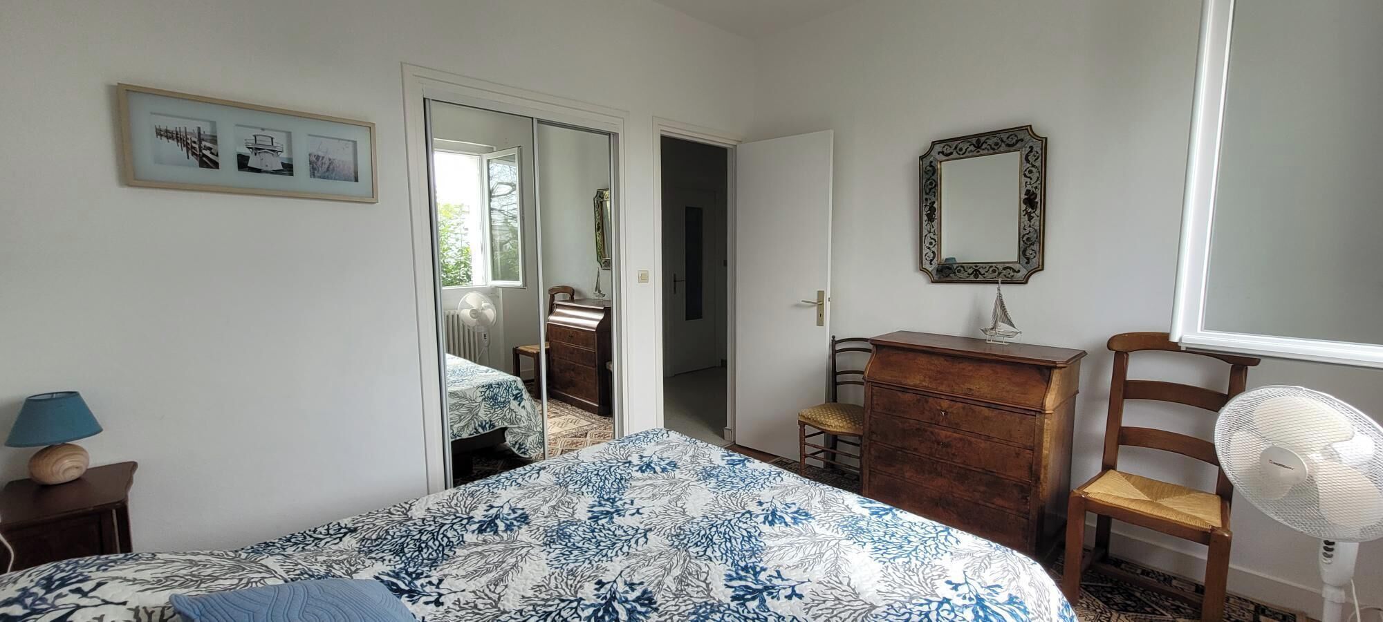 A bedroom with a bed, dresser, chair, and a fan.