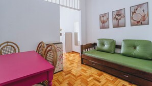 A room with a wooden herringbone floor, a green sofa with a wooden frame, a pink table, wicker chairs, and a white cabinet. - Apto Confort vel Tima Localiza o e pet Friendly (Teresópolis)