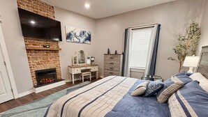 Une chambre avec une cheminée, un lit avec une literie à rayures, une commode et un téléviseur fixé au mur.