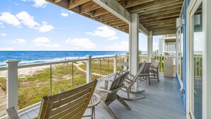 Una terraza techada con sillas y mesa de madera, con vistas a una playa y al océano.