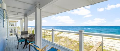 A covered outdoor area with a table and chairs, overlooking a beach and ocean.