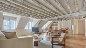 Un loft espacioso con vigas de madera a la vista, un área de comedor con televisor y grandes ventanales.