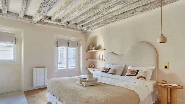 Un dormitorio con una cama grande, vigas de madera en el techo, un radiador y una mesita de noche con lámpara.