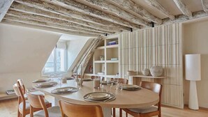 Un comedor con una mesa redonda dispuesta para seis personas, sillas de madera y un armario blanco con estantes.