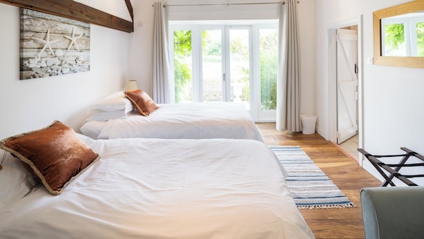 Un dormitorio con dos camas, piso de madera, un ventanal con cortinas y un cuadro en la pared.