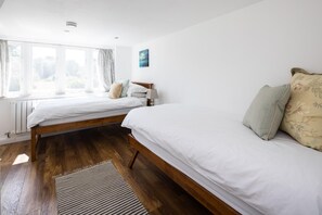 A room with two single beds, a window with curtains, a radiator, and a wooden floor. - The Dovecote 3-bed Cottage, Rowden Manor (Chippenham)
