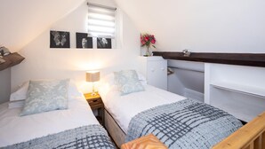 A bedroom with two beds, a nightstand, a lamp, a dresser, and a window with blinds. - The Dovecote 3-bed Cottage, Rowden Manor (Chippenham)