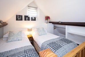 A bedroom with two beds, a nightstand, a lamp, a dresser, and a window with blinds. - The Dovecote 3-bed Cottage, Rowden Manor (Chippenham)