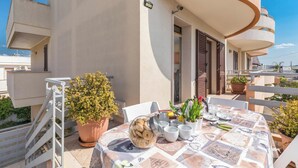 A balcony with a table set for dining, potted plants, and a view of the surrounding buildings. - Appartamento Terrazza by BarbarHouse (Porto Cesareo)