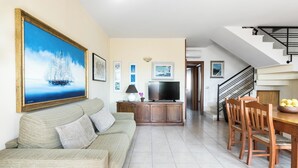 A living room with a sofa, TV, and dining area with chairs and a table. - Appartamento Terrazza by BarbarHouse (Porto Cesareo)